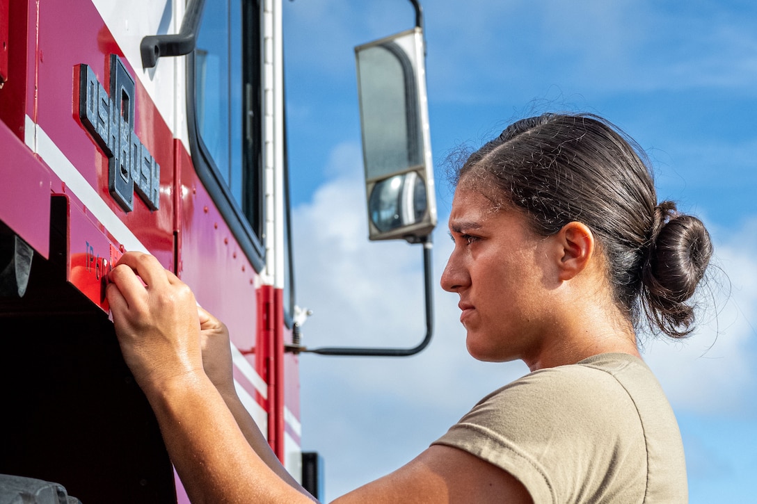 A close-up of a focused airman putting a piece of tape on a partially visible firetruck.
