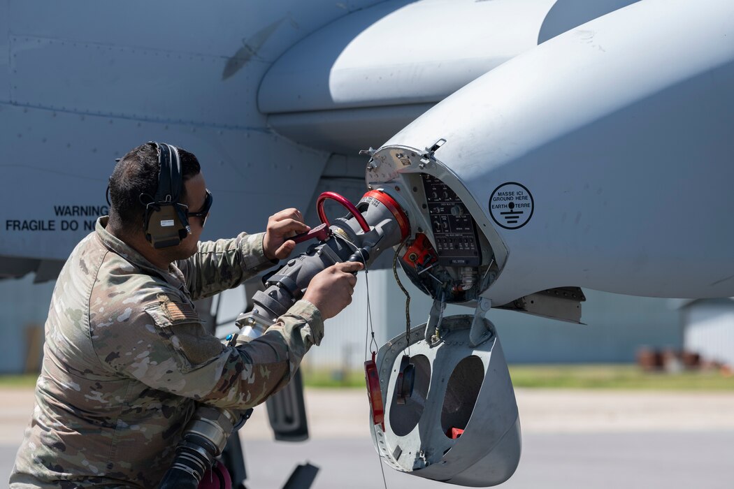 A person holding a fuel hose to the gas intake on an A-10C.