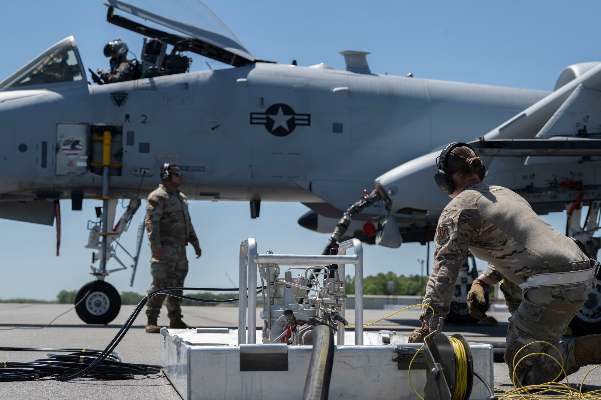 long shot of a person crouched down next to a VIPER Kit, while in the background there's a person refueling an A-10C Thunderbolt II.