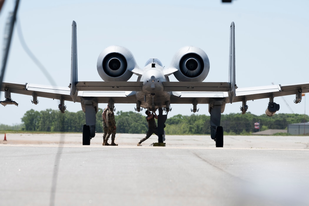 An A-10C Thunderbolt II with people working under it.
