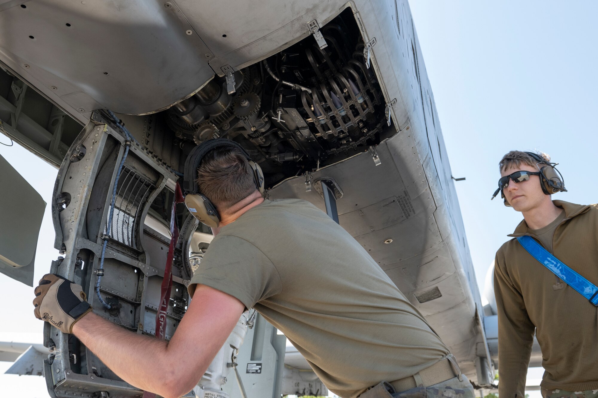 Two people looking at the weapons system under an A-10C Thunderbolt II.