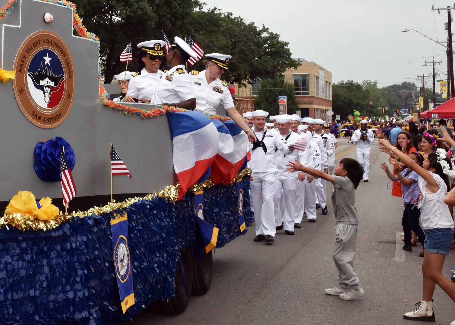SAN ANTONIO - (April 26, 2024) – Capt. Jennifer Buechel (Nurse Corps), commanding officer, Naval Medical Research Unit (NAMRU) San Antonio, gives a child a Navy Fiesta Medal during the Battle of Flowers Parade held during Fiesta San Antonio. The Battle of Flowers Parade is the oldest event and largest parade of Fiesta San Antonio attracting crowds of more than 350,000. Leading more than 100 Sailors in the parade was Rear Adm. Walter Brafford, commander, Naval Medical Forces Support Command (NMFSC). Joint Base San Antonio is proud to be part of the diverse and vibrant community of San Antonio also known as Military City USA. (U.S. Navy Photo by Burrell Parmer, Naval Medical Research Unit San Antonio Public Affairs/Released)