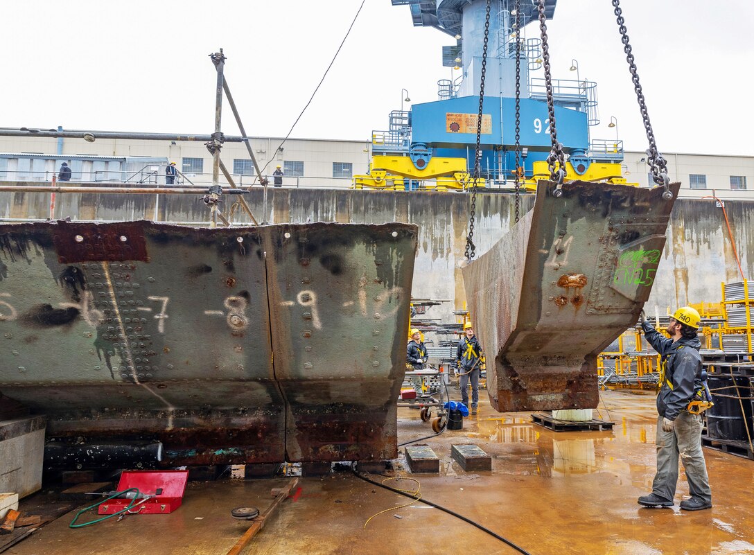 A team of riggers from Code 740, Riggers, help guide a section of concrete ballast from old Caisson 3's keel as it's lifted by crane, March 27, 2024, up and out of Dry Dock 3 at Puget Sound Naval Shipyard & Intermediate Maintenance Facility in Bremerton, Washington. (U.S Navy photo by Wendy Hallmark)