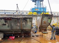 A team of riggers from Code 740, Riggers, help guide a section of concrete ballast from old Caisson 3's keel as it's lifted by crane, March 27, 2024, up and out of Dry Dock 3 at Puget Sound Naval Shipyard & Intermediate Maintenance Facility in Bremerton, Washington. (U.S Navy photo by Wendy Hallmark)