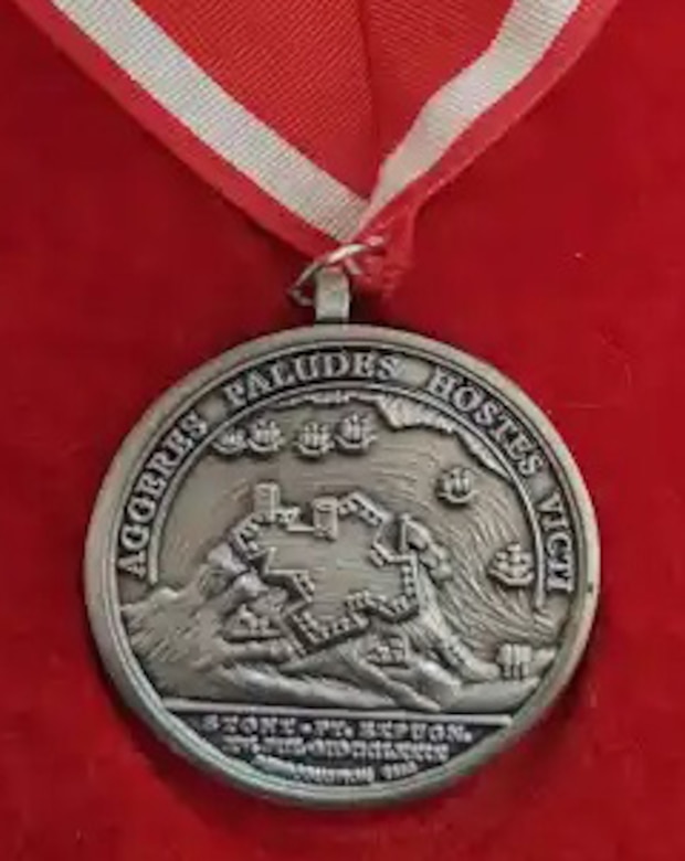The reverse of the de Fleury Medal has (in Latin): “Fortifications, Marshes, Enemies Overcome.” In the center the fortress at Stony Point is depicted with both turrets and a flag flying. At the base of the hill are two shore batteries, one of which is firing at one of six vessels on the Hudson River. Beneath the fort is the legend: “Stony Point Carried by Storm, July 15, 1779.”