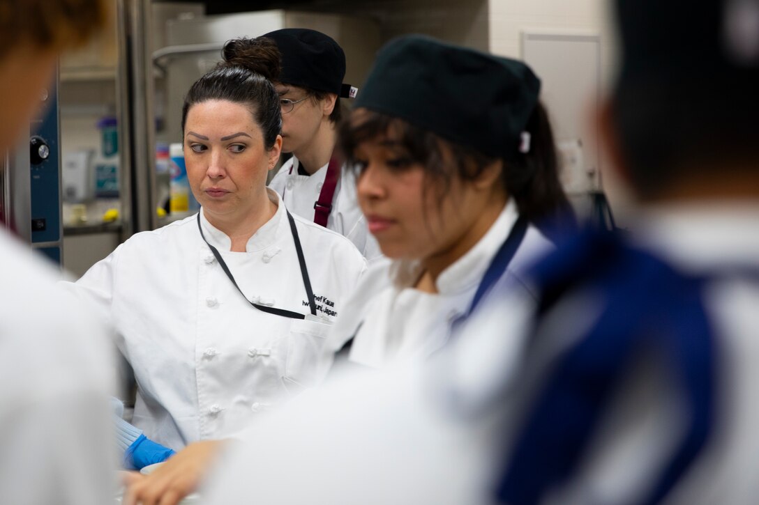 Chef Karri Selby, a chef at Matthew C. Perry High School, watches her students prepare dishes during the Food Pantry Cooking Competition held by M.C. Perry High School at Marine Corps Air Station Iwakuni, Japan, April 18, 2024.The students of M.C. Perry High School were tasked with creating unique dishes with non-perishable items such as spam, canned black beans, and rice, which were provided by the Iwakuni Food Pantry, to show creative ways to make tasty dishes with common, shelf-stable ingredients.  (U.S. Marine Corps photo by Lance Cpl. Micah Taylor)