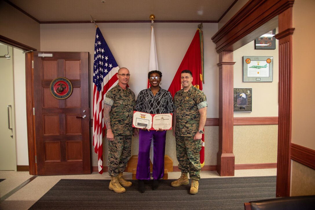U.S. Marine Corps Cpl. Cyrielle Moutsinga, an aviation operations specialist with Marine Aircraft Group 12, 1st Marine Air Wing, and a native of New York, center, poses for a photo with Sgt. Maj. Jody Armentrout, the sergeant major of Marine Corps Air Station Iwakuni, and a native of Texas, left, and Col. Richard Rusnok, the commanding officer of MCAS Iwakuni, and a native of Pennsylvania, after being awarded the March 2024 Impact Iwakuni award at MCAS Iwakuni, Japan, April 24, 2024. The Impact Iwakuni award is presented monthly to recipients that make a significant positive impact on the community. Moutsinga was presented the award in part to recognize her volunteer work and mentorship as the MAG-12 Single Marine Program representative for the past 17 months. (U.S. Marine Corps photo by Cpl. Calah Thompson)