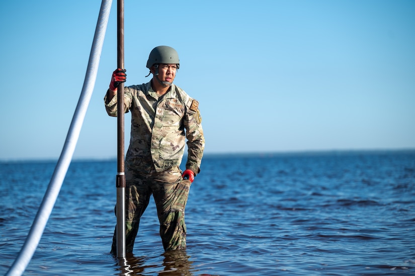An airman holds a pole while standing in a body of water.