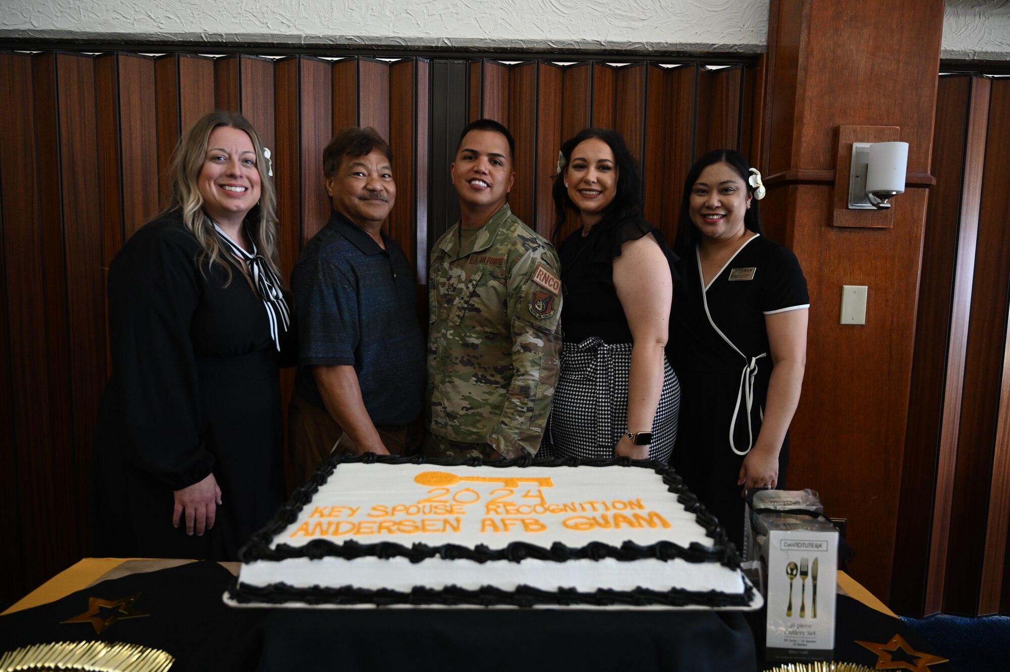 Members of the Key Spouse program along with an Airman pose for a group photo behind a cake.
