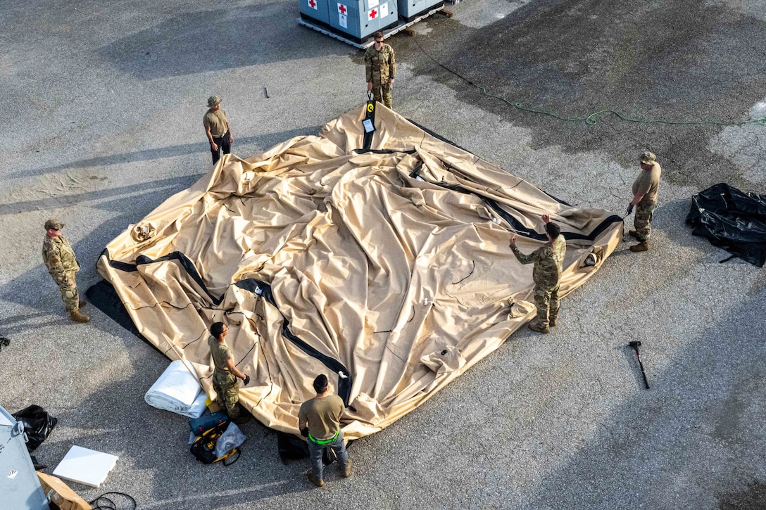 A group of airmen seen from above stand around a large tent that lies flat on the ground.