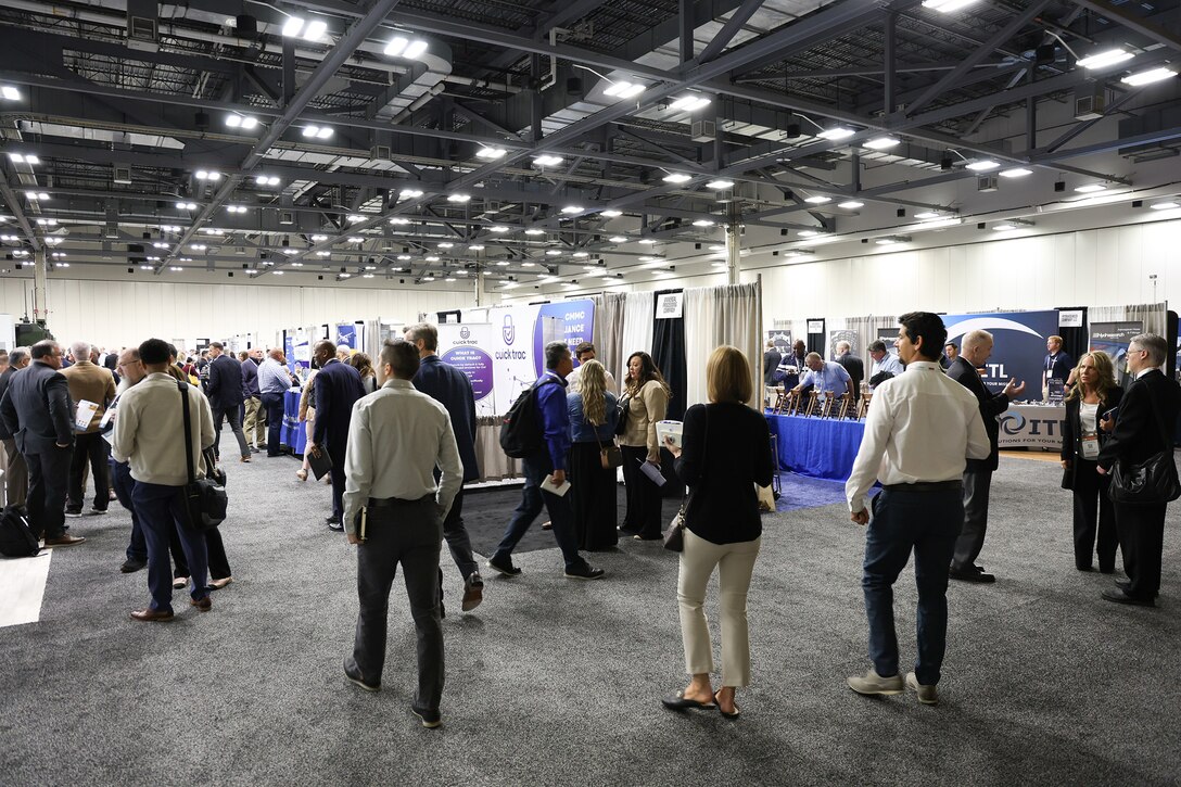 Many people in business attire wander around a large exhibition hall filled with booths.