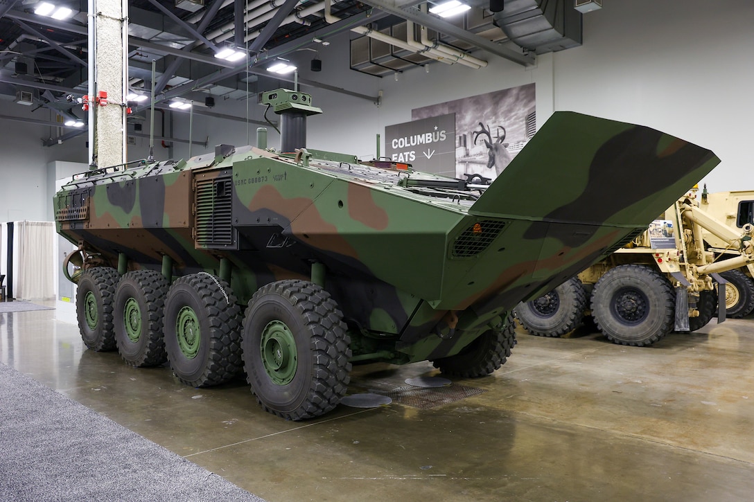 A large tan military vehicle sits in an exhibition hall.