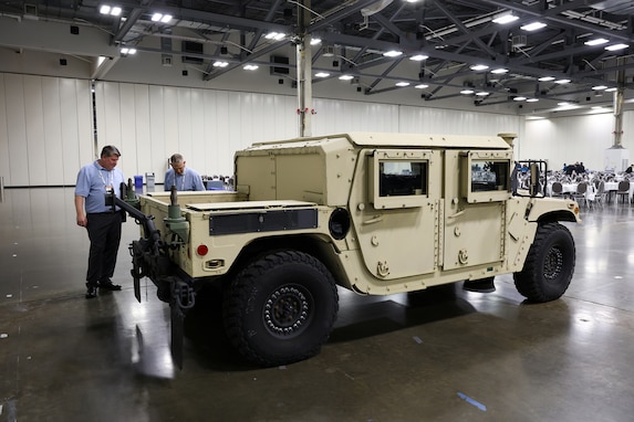 A large tan military vehicle sits in an exhibition hall.