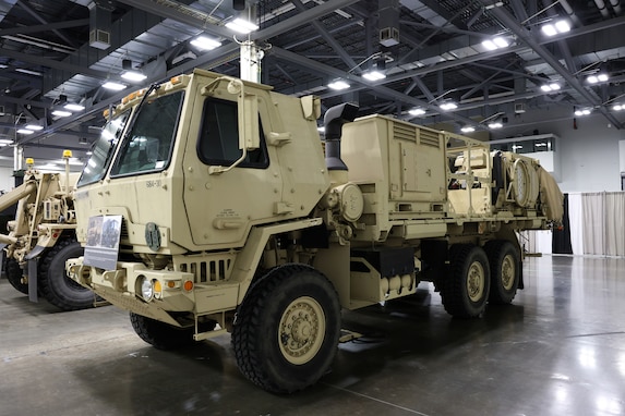A large tan military vehicle sits in an exhibition hall.