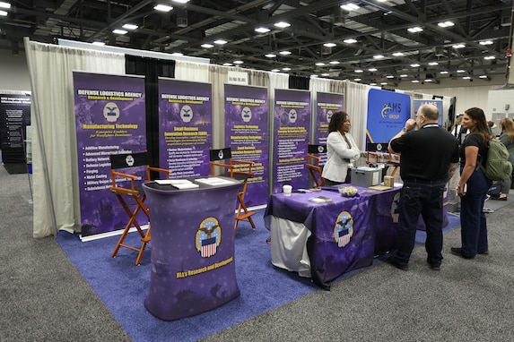 A group of people in business attire, men and women, at a booth in a exhibition hall.