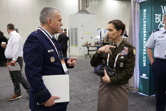 A light skinned dark haired woman in a Army uniform talks with a light skinned man with short graying hair in a Air Force uniform.