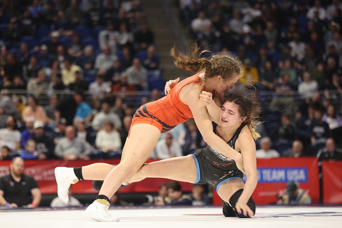 A wrestler lunges toward another wrester who is down on a mat during a competition.