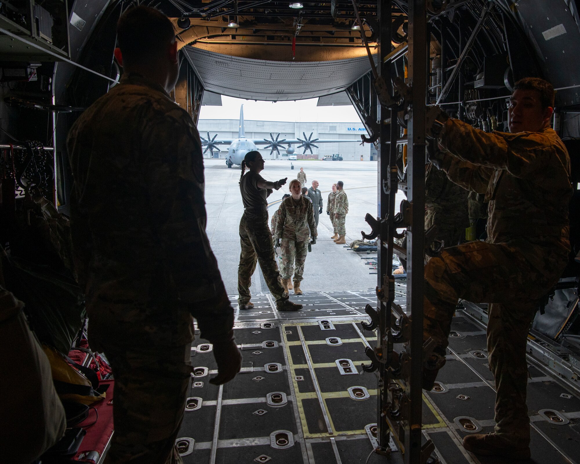 people in military uniforms stand on an open aircraft ramp while parked on a flight line