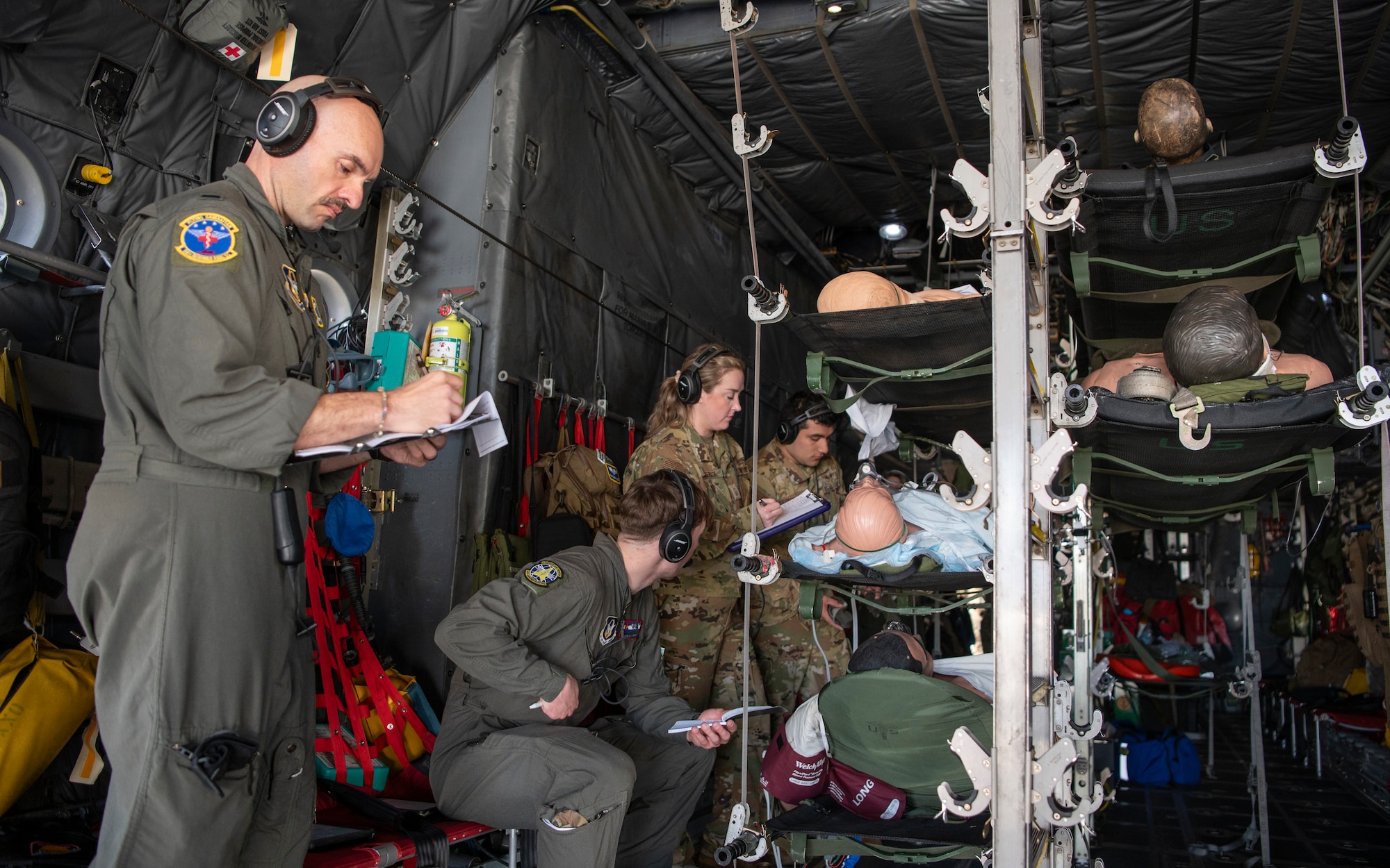 people in military uniforms practice medical procedures on manikins while inside an aircraft