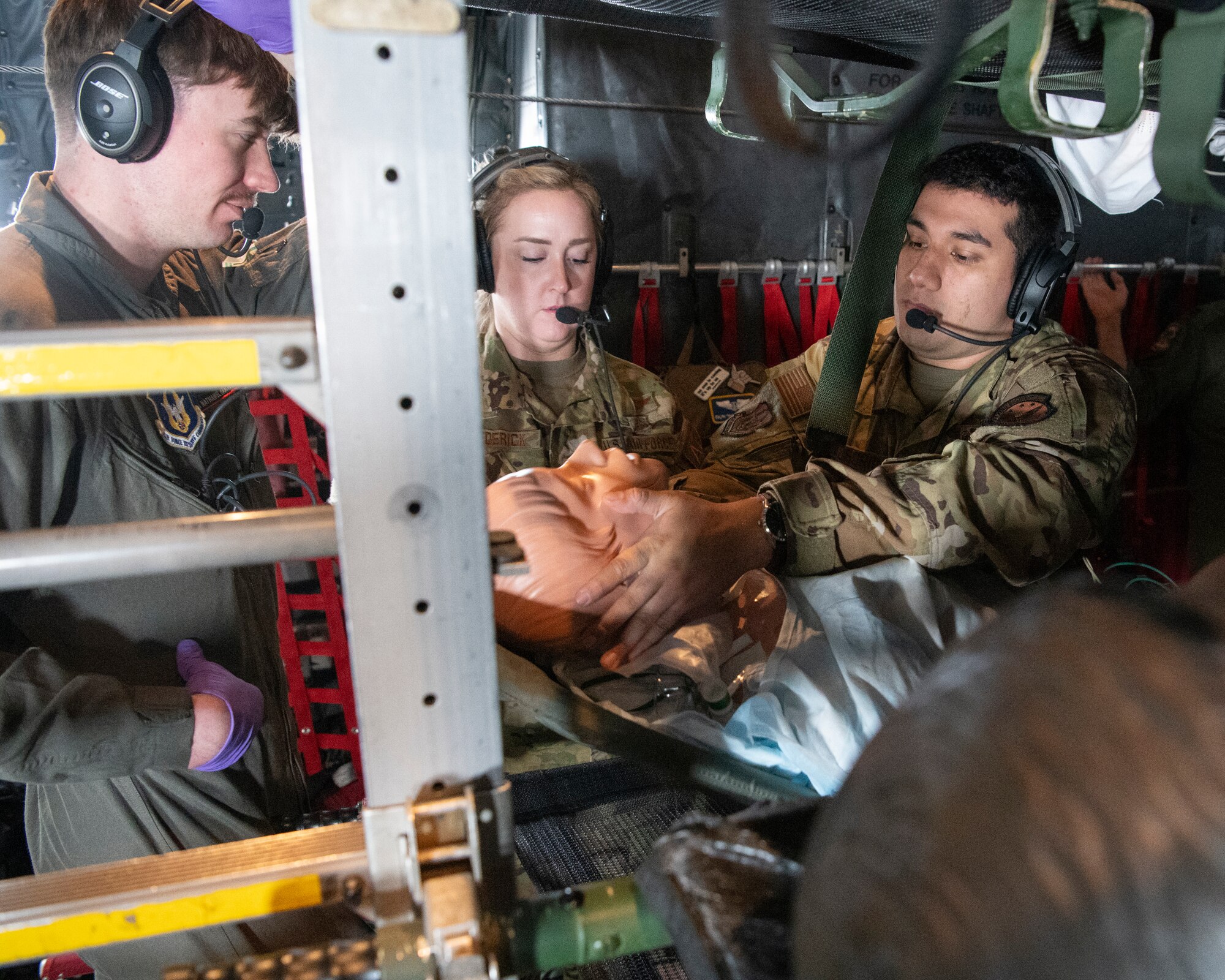 three people in military uniforms practice medical procedures while inside an airplane