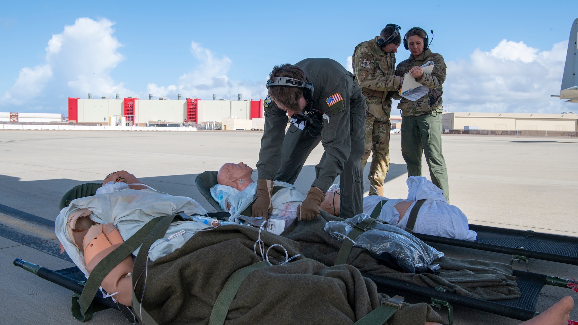 people in military uniforms stand beside a medical litter while outside on a flight line