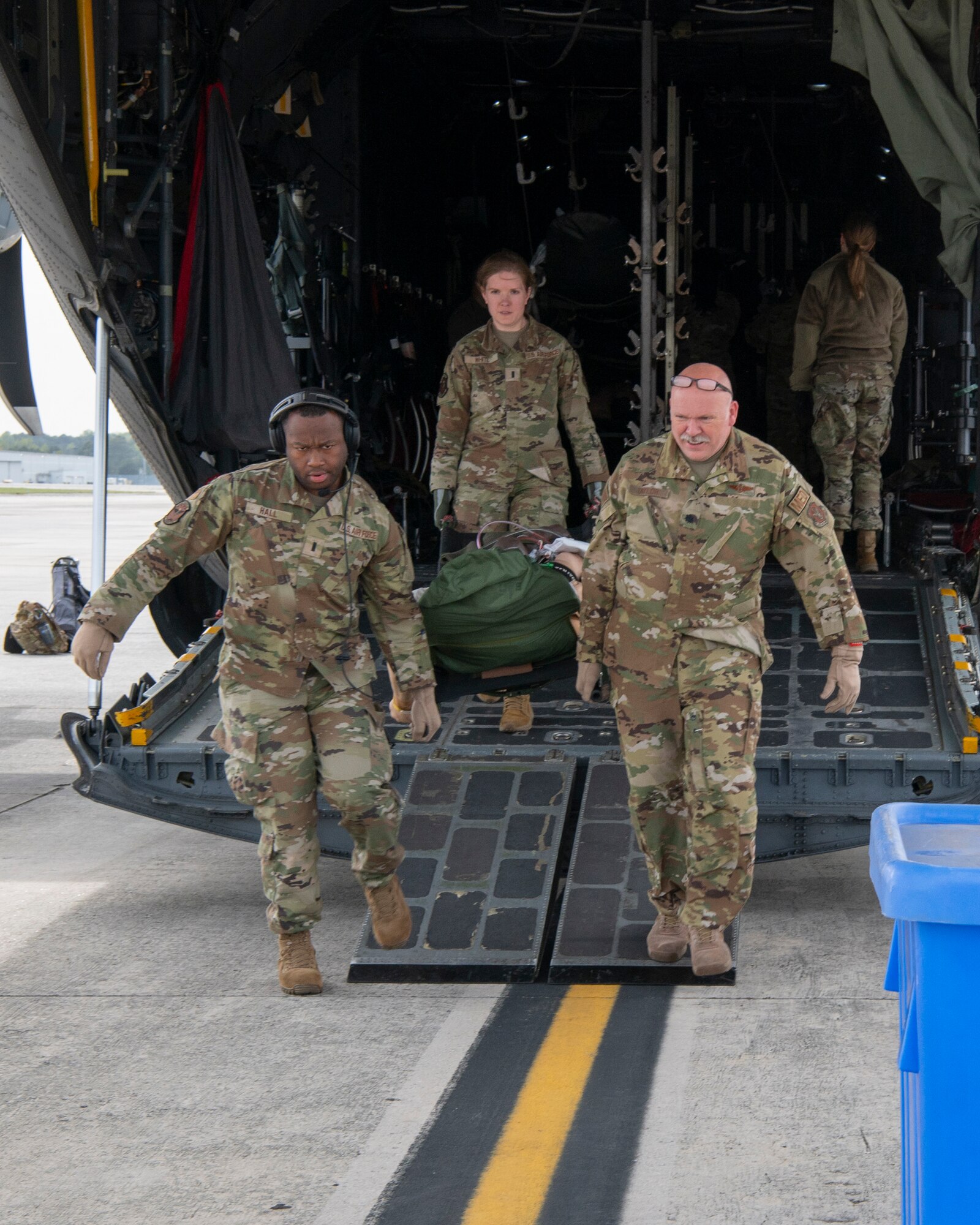 three people in uniform carry a medical litter out the ramp of an airplane