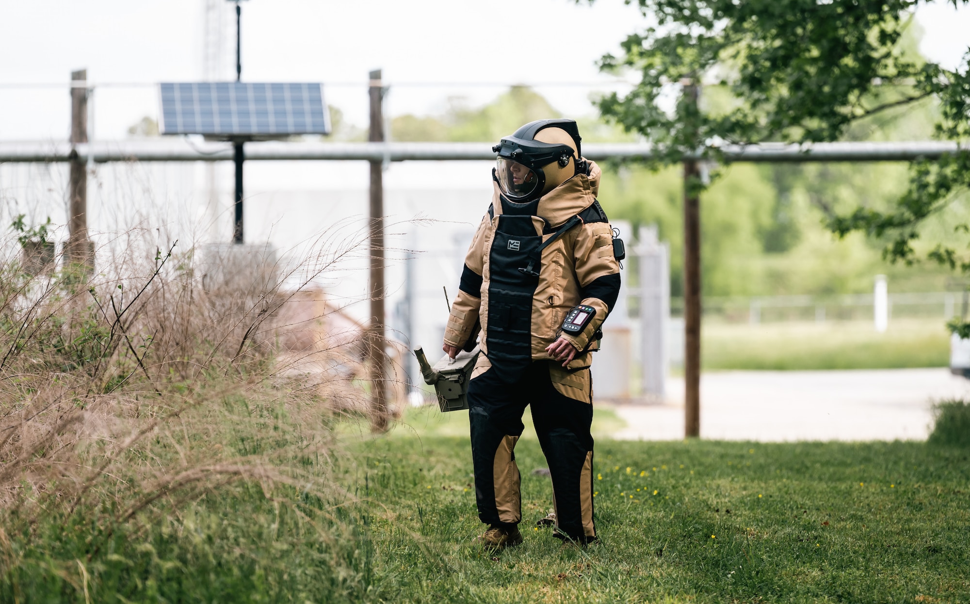 A man in a bomb suit surveys the grass for a downed drone