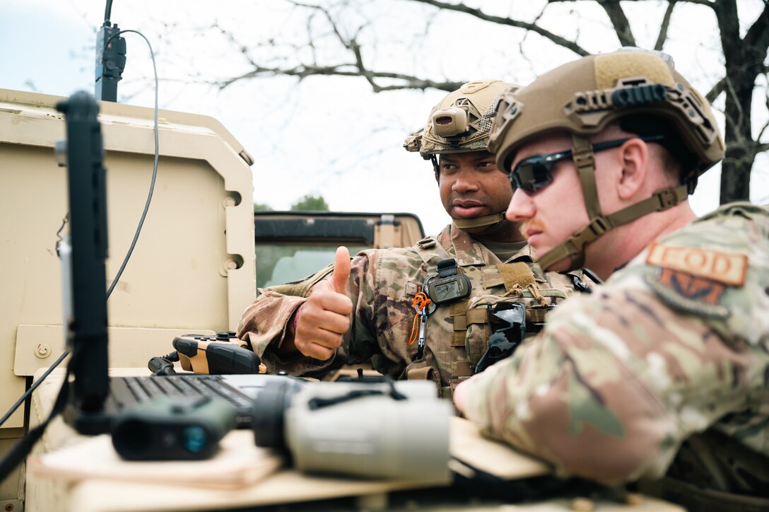 Two male Airman look at a computer with tactical helmets on