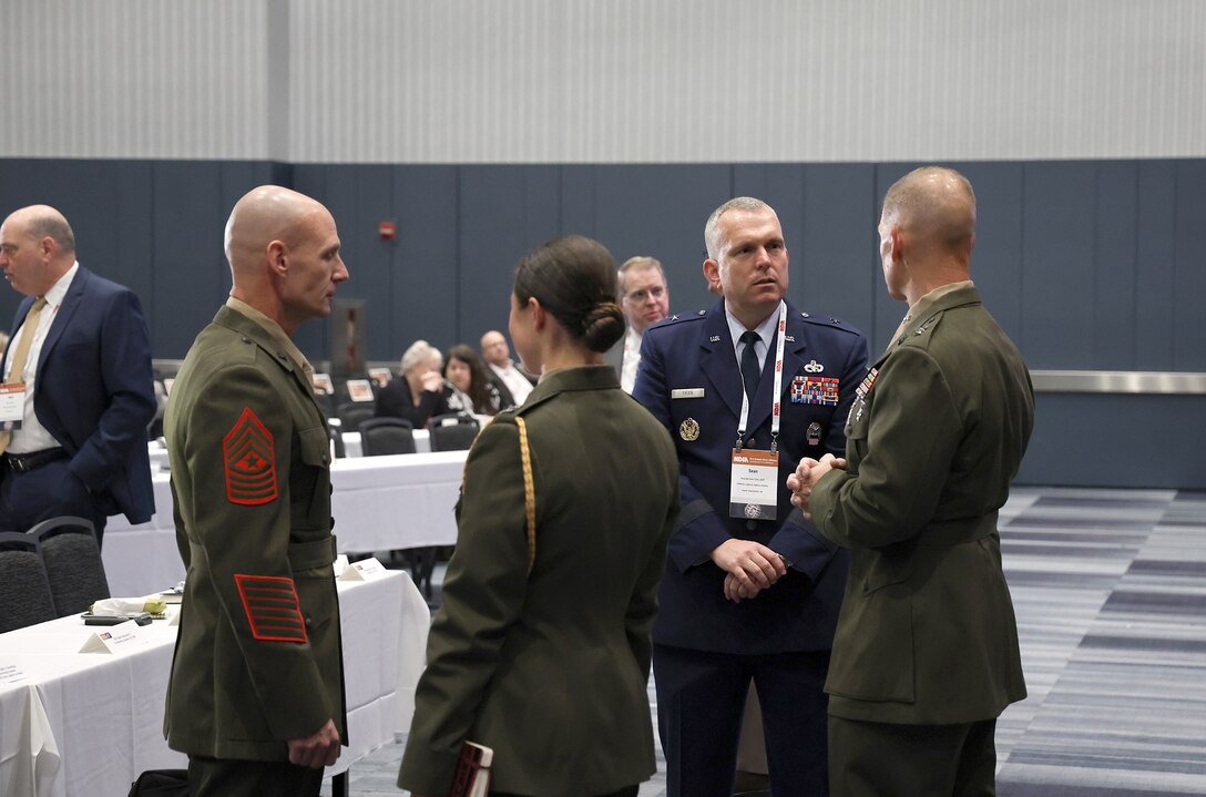 A man in a blue Air Force uniform speaks with several Marines in dress uniforms.