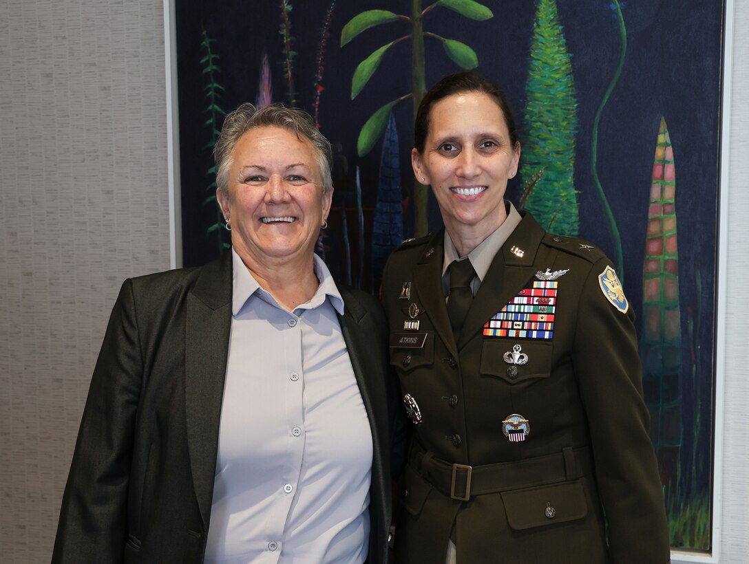 Two women smile for the camera. One is in an Army uniform and one is not. The other woman is wearing a business suit.