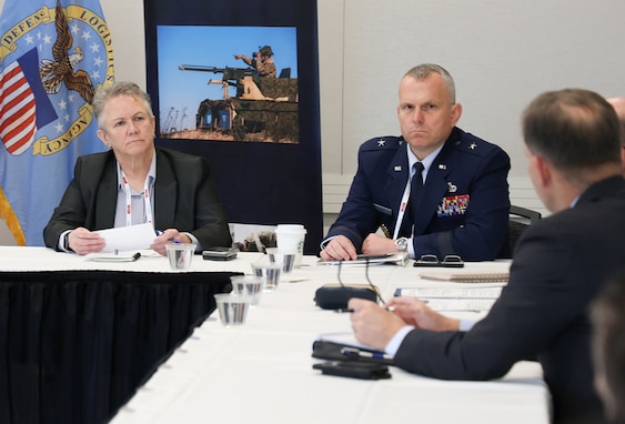 A man in a Air Force uniform a man in a business suit and a woman in a business suit are seated at a white table.