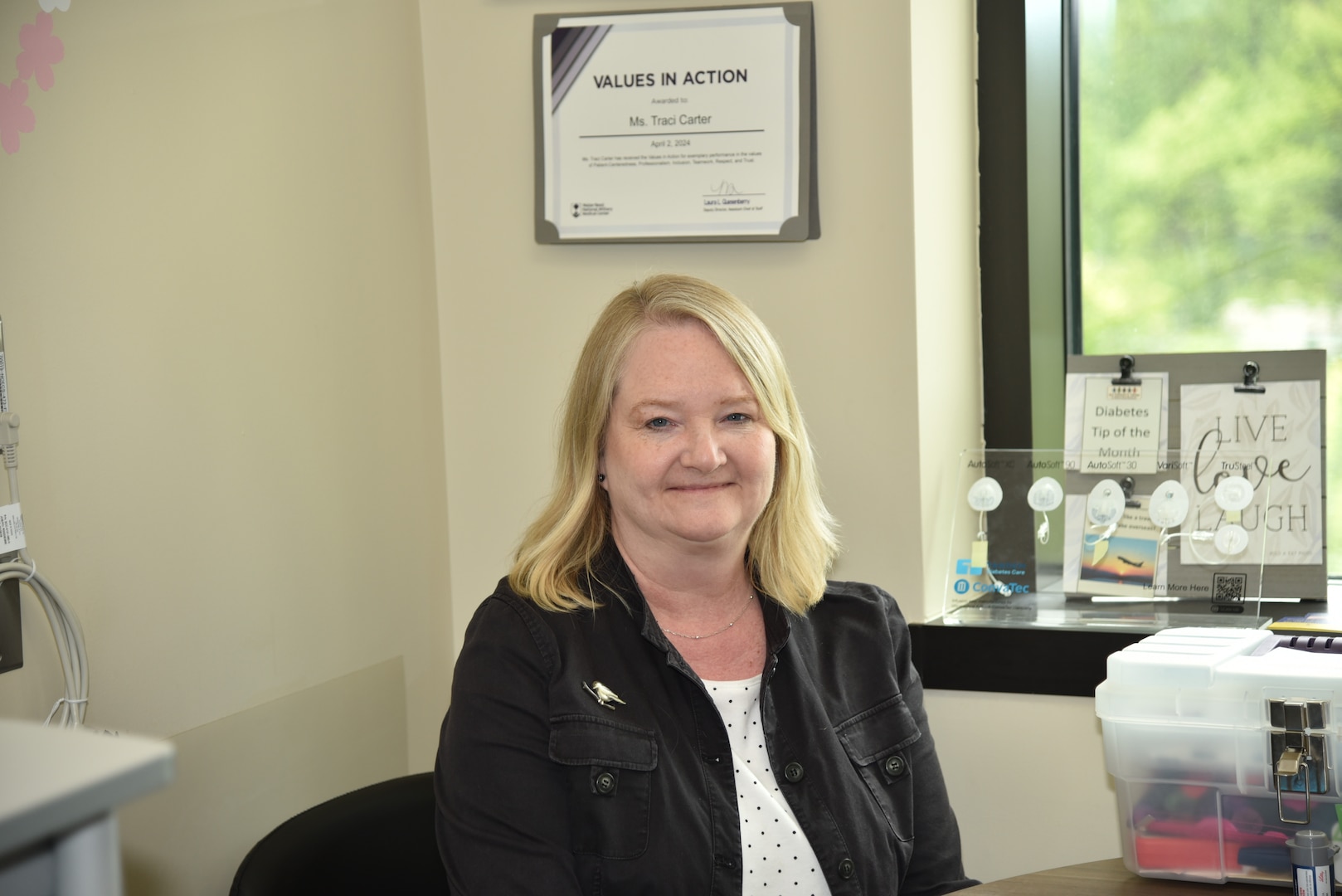 Nurse Educator Traci M. Carter smiles in her office on April 23, 2024 at Walter Reed amid her Values in Action Award and medical toolkit before meeting her next onsite patient in Bethesda, Maryland.