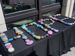 Colorful painted rocks spelling "HOPE" are laid out on a table with a black tablecloth.
