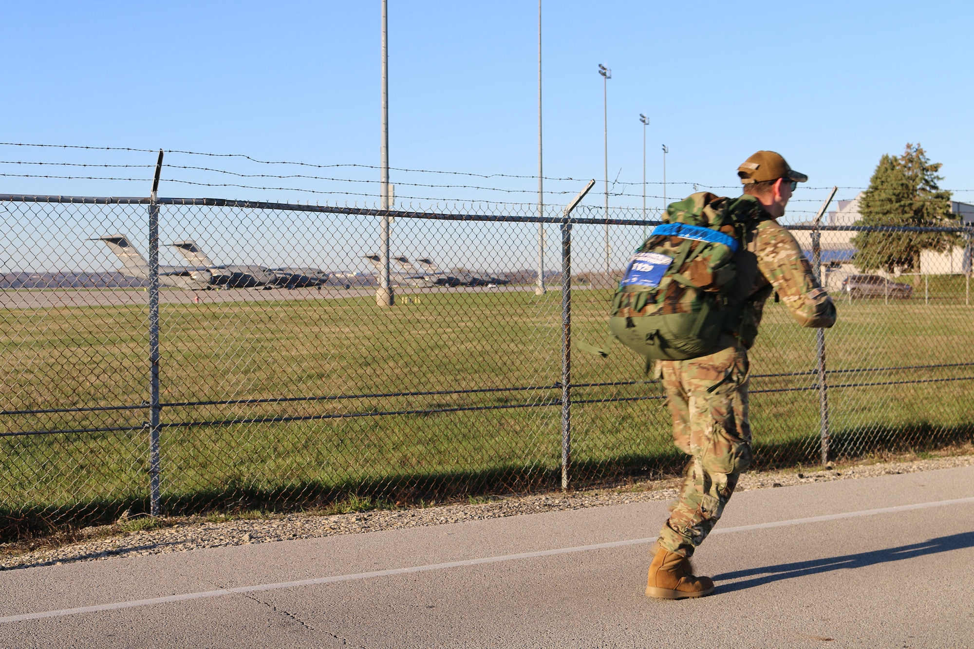 Senior Airman Zechariah Gerardi, 445th Airlift Wing command post, passes by the flighline with the wing's C-17 Globemaster III aircraft featured as a backdrop during the Norwegian foot march hosted by the 88th Security Forces Squadron April 6, 2024. Gerardi was among 100 participants of the march with each participant carrying a backpack that weighed at least 25 pounds around the course.
