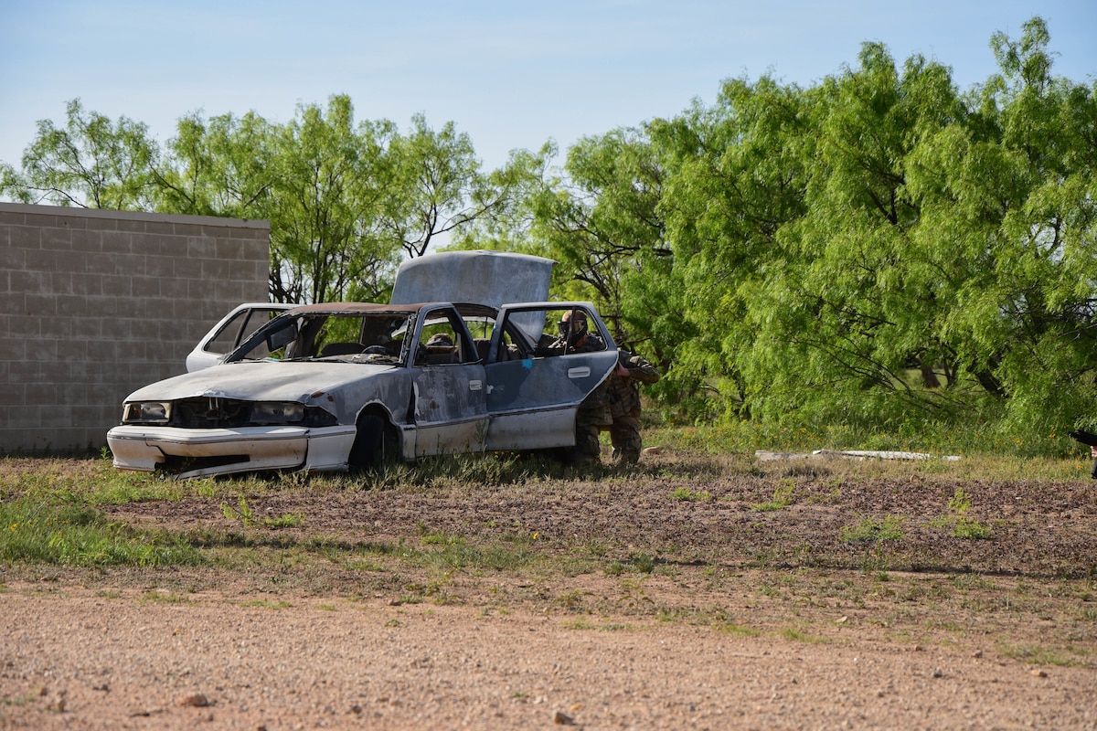 Expeditionary Readiness Training Opposing Force volunteers fire paintballs while taking cover behind a car during the field operations exercise portion of ERT course 24-7, Goodfellow Air Force Base, Texas, April 12, 2024. During the exercise, the OPFOR engaged with ERT students in various scenarios to assess the class’s concept retainment and execution capabilities. (U.S. Marine Corps photo by Cpl. Jessica Roeder)