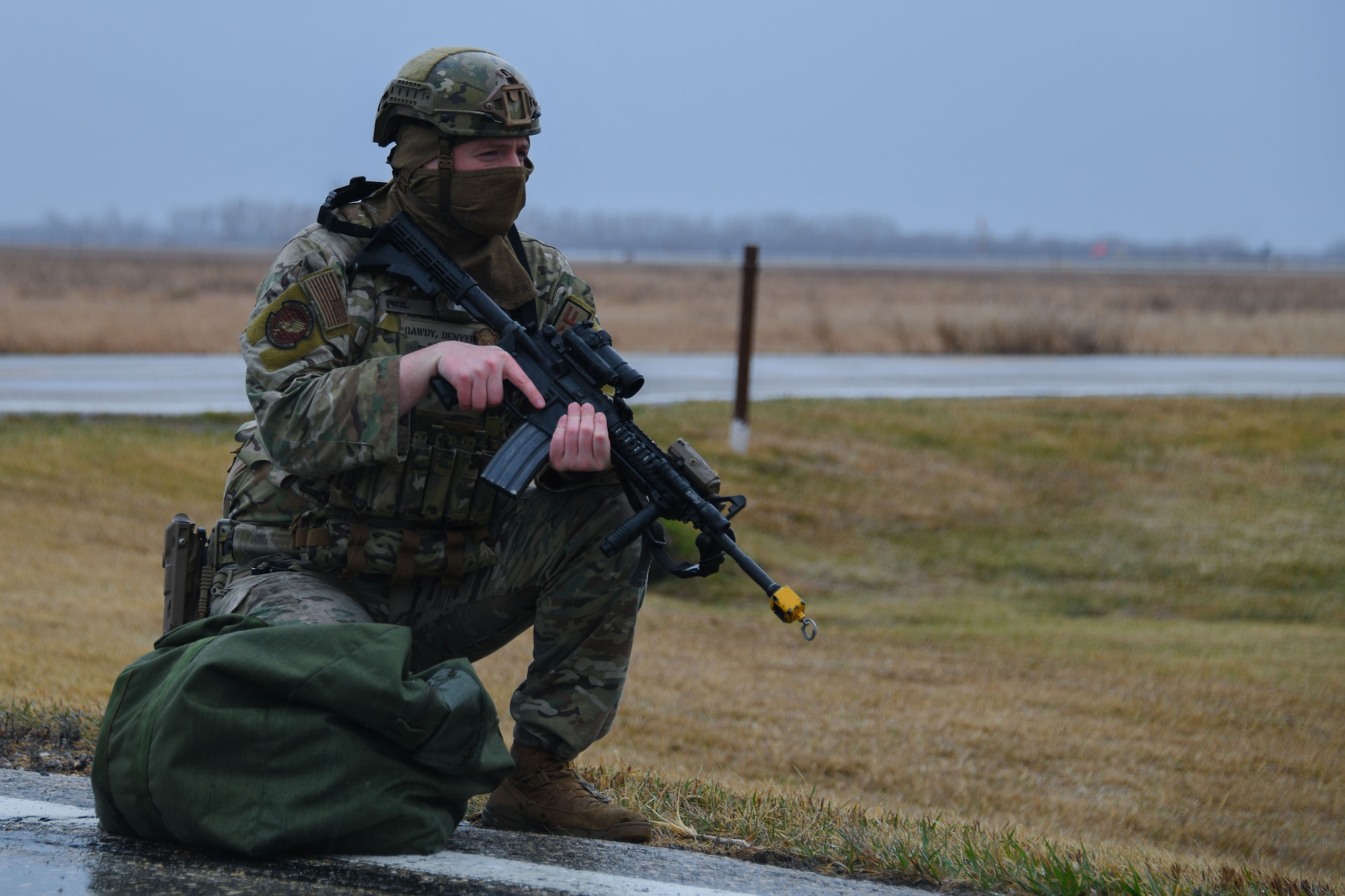 Armed military member kneels on the side of a road.