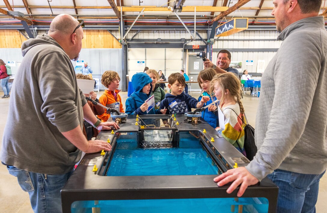 Theron Bergland, general foreman, Shop 64, Shipwrights, and Steven Middendorf, docking zone manager, Code 240, Engineering and Planning, get help pumping out a dry dock mock-up from a group of students, April 16, 2024, at the Kitsap Water Festival in Bremerton, Washington. (U.S. Navy photo by Wendy Hallmark)