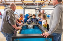 Theron Bergland, general foreman, Shop 64, Shipwrights, and Steven Middendorf, docking zone manager, Code 240, Engineering and Planning, get help pumping out a dry dock mock-up from a group of students, April 16, 2024, at the Kitsap Water Festival in Bremerton, Washington. (U.S. Navy photo by Wendy Hallmark)
