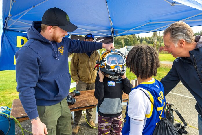 Petty Officer 1st Class John Miller, Puget Sound Naval Shipyard & Intermediate Maintenance Facility, Bangor, Dive Locker, helps students try on a helmet, April 16, 2024 during the annual Kitsap Water Festival in Bremerton, Washington. (U.S Navy photo by Wendy Hallmark)