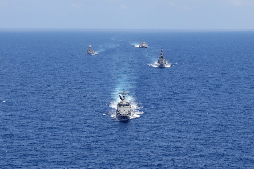 Four military ships transit open waters in formation.