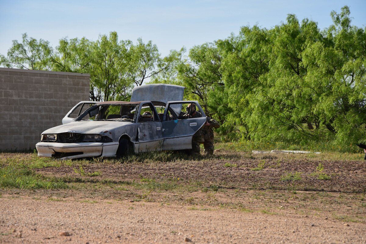Expeditionary Readiness Training Opposing Force volunteers fire paintballs while taking cover behind a car during the field operations exercise portion of ERT course 24-7, Goodfellow Air Force Base, Texas, April 12, 2024. During the exercise, the OPFOR engaged with ERT students in various scenarios to assess the class’s concept retainment and execution capabilities. (U.S. Marine Corps photo by Cpl. Jessica Roeder)