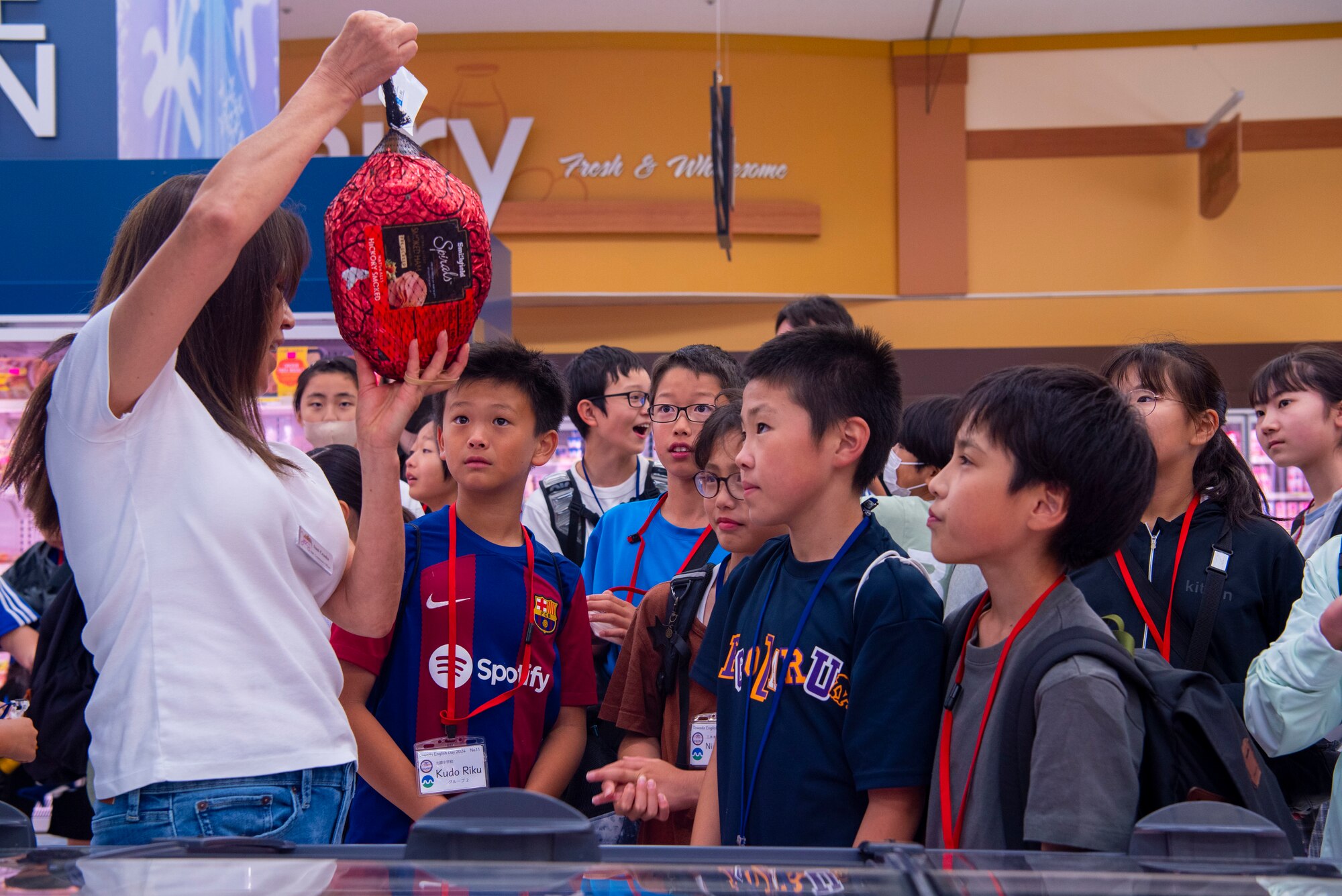 Suntok Crusha, left, Misawa Commissary assistant officer, shows Towada Elementary School students a ham and other food items as they practice their English during a Junior English tour at Misawa Air Base, Japan, July 23, 2024.