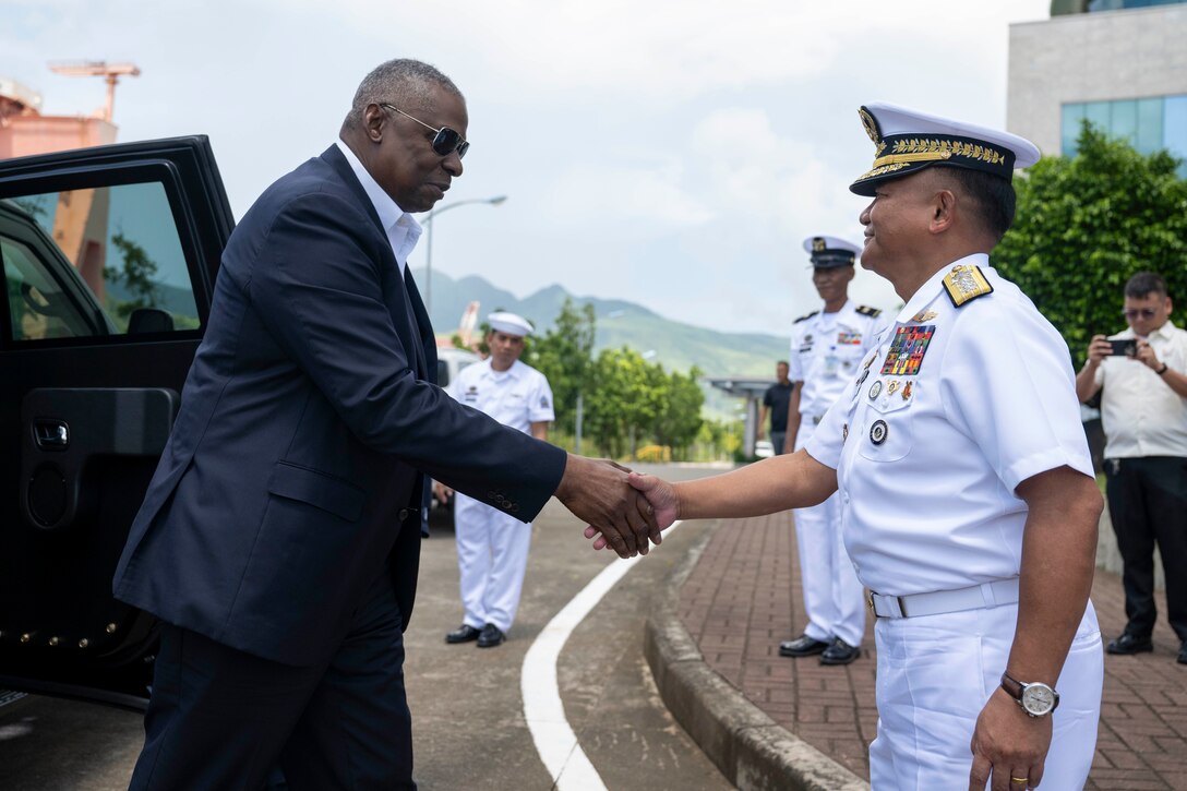 Defense Secretary Lloyd J. Austin III shakes hands with a high-ranking Philippine sailor while on a road next to an open vehicle.