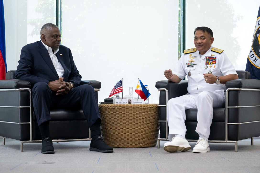 Defense Secretary Lloyd J. Austin III sits next to a high-ranking Philippine sailor wearing white, while a side table between them displays the American and Philippine flags.