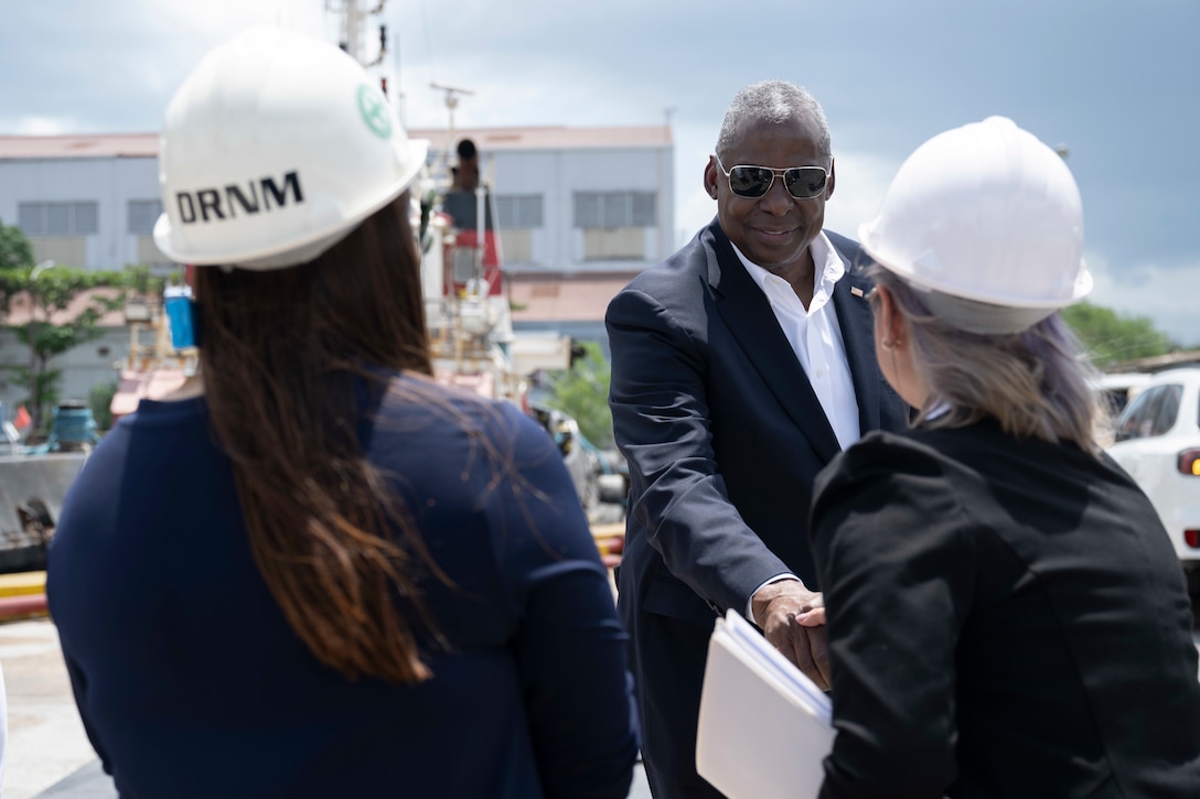 Defense Secretary Lloyd J. Austin III shakes hands with two employees in business suits and hardhats.