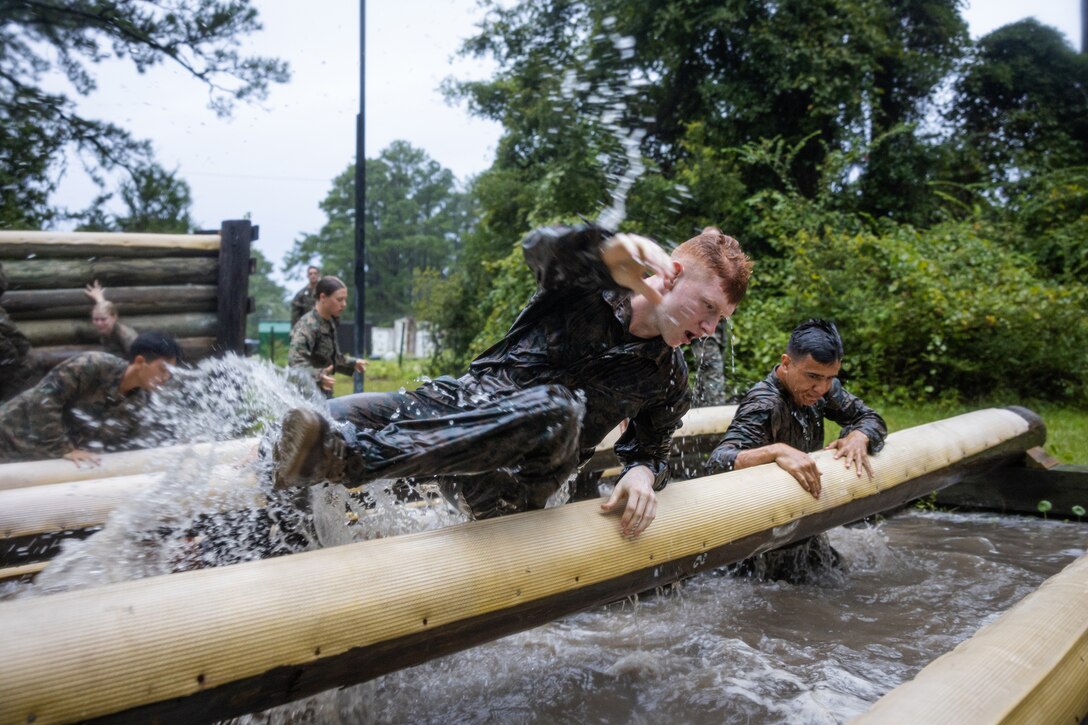 Navy midshipmen navigate through logs over water during training.