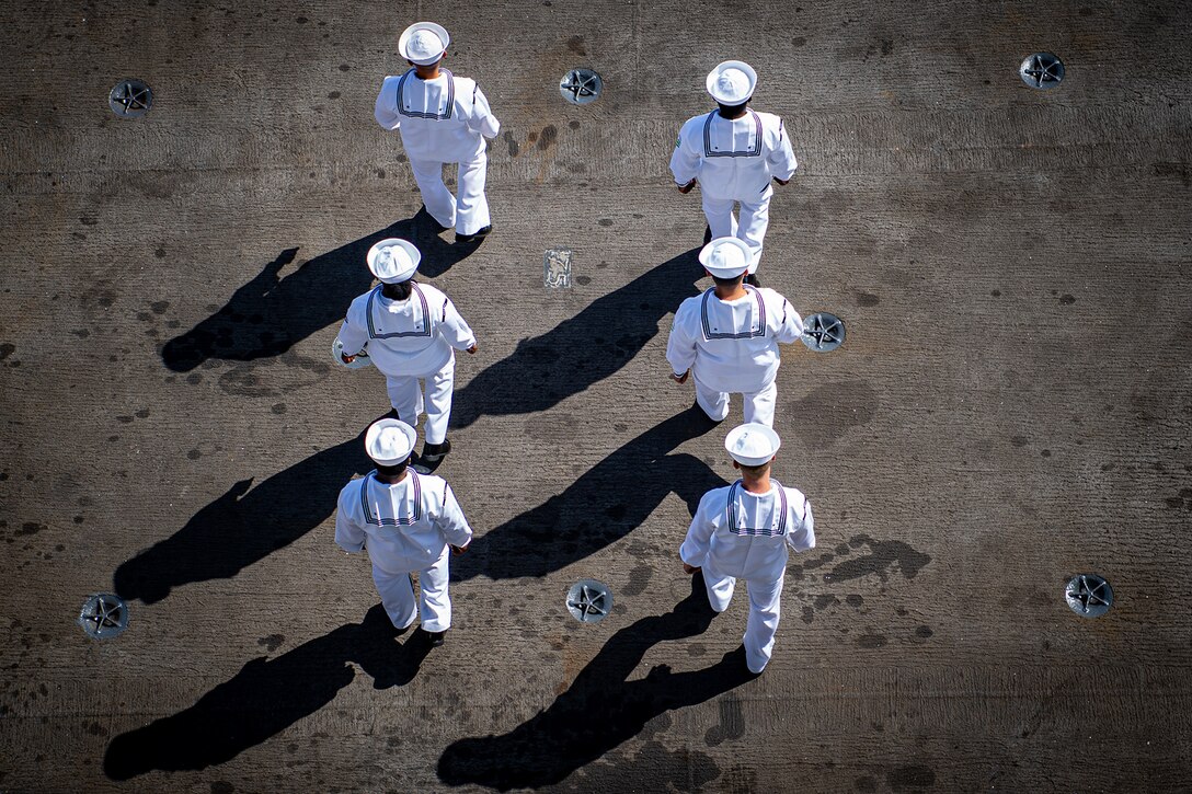 Aerial view of six sailors standing on the flight deck of a ship during daylight.