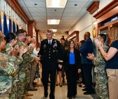 Gen. Daniel Hokanson and his wife, Kelly Hokanson, walk through a hallway in the Pentagon through lines of people clapping on either side of the hallway.