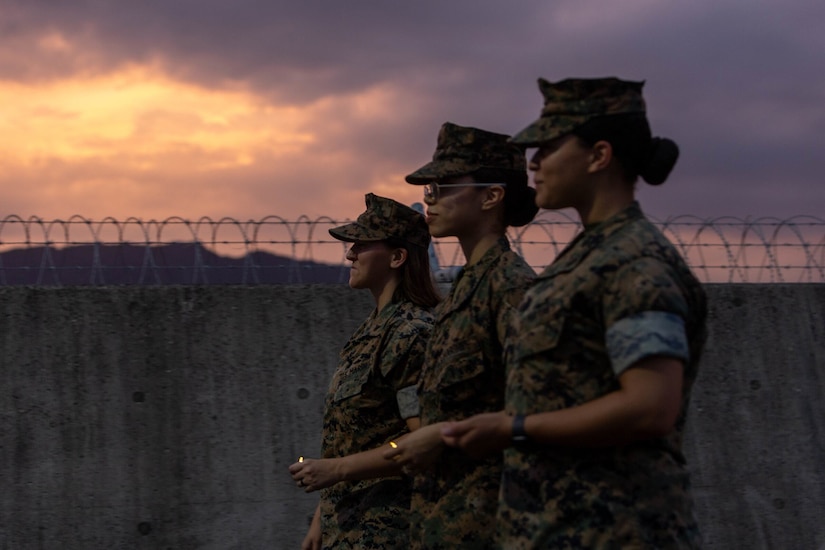 Three marines walk holding lighters at twilight.