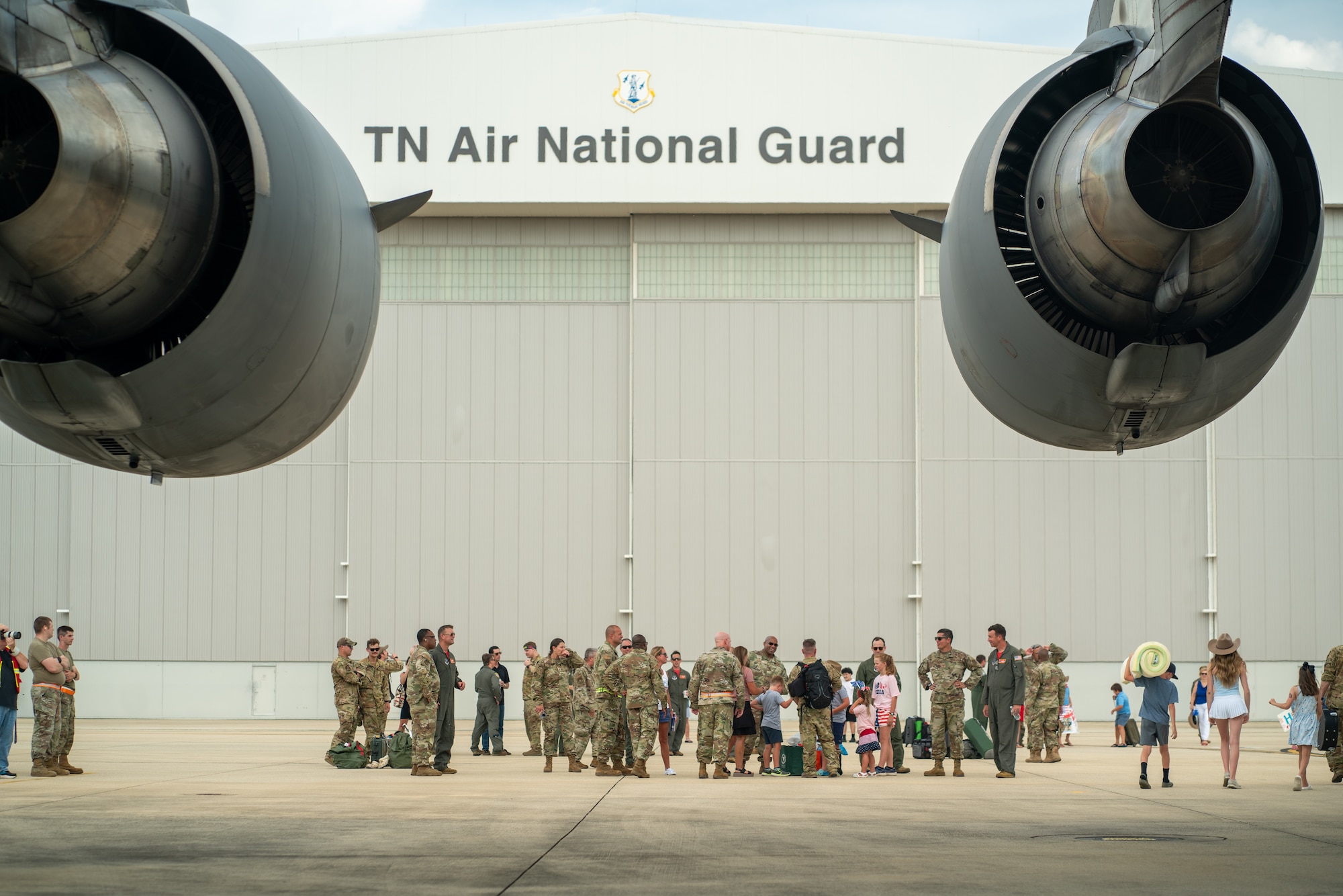 Airmen and civilians on a flight line in front of a hangar.